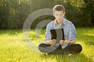 Boy holding tablet PC on green grass lawn