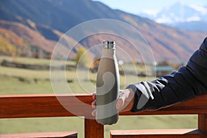 Boy holding thermo bottle with drink in mountains on sunny day, closeup