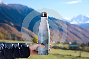 Boy holding thermo bottle with drink in mountains on sunny day, closeup