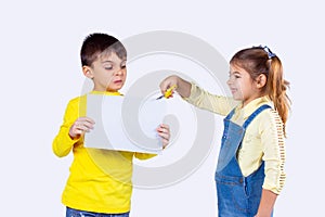 The boy holding a white clean paper in his hand and girl tries to cut the paper carefully with the help of scissors.