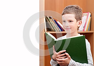 Boy holds book against bookshelf
