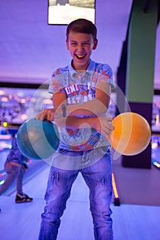 A boy holds bowling balls posing for the camera