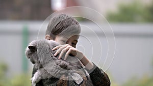 Boy holds a british cat in his arms and strokes her outdoors