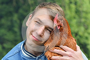 The boy holds a chicken in his hands and hugs her