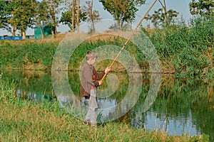 A boy holds a fishing rod over the water for fishing