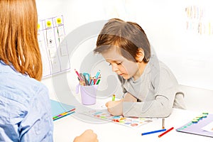 Boy holds pencil and colors the shapes on paper