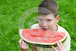 The boy holds a slice of red watermelon and wants to bite off a slice, looking forward