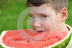 Boy holds a slice of red watermelon and wants to bite off a slice, side view close-up