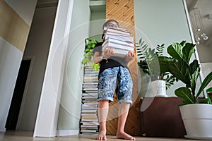 A boy holds a stack of books against the background home library.