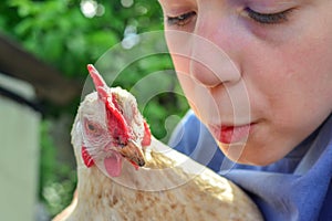 The boy holds a white chicken in his hands and kisses her