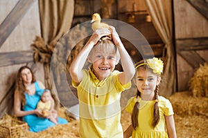 boy holds a yellow duckling on his head, and his sister stands next to him, both laughing