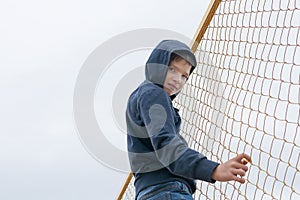 A boy in a hood climbed a fence from a net, street children