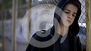 Boy in hoodie leaning on fence, orphan in boarding school, confinement