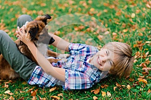 Boy hugging dog and plyaing with in the fall, city park