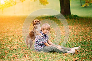 Boy hugging dog and plyaing with in the fall, city park