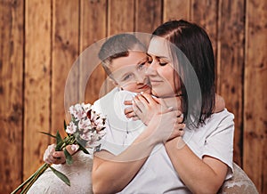 Boy hugs his mother and gives her flowers. Tenderness