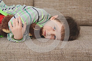 Boy hugs his teddy bear and lying on the sofa