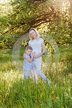 A boy hugs a pregnant mother `s stomach. photo session of pregnant women in the summer