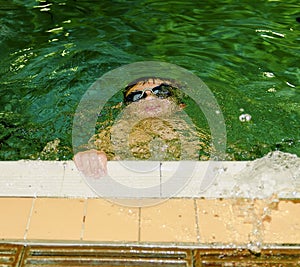 Boy in the indoor public pool. Child with swimmng goggle dives.
