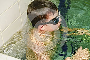 Boy in the indoor public pool. Portrait of child with swimmng goggles.