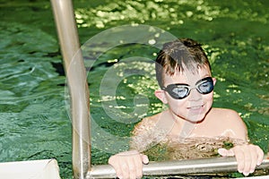 Boy in the indoor public pool. Portrait of child with swimmng goggles. Boy goes up on ladder.