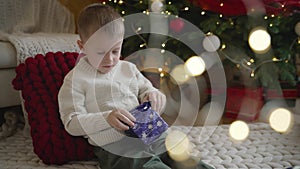 A boy in a jacket examines a Christmas New Year's gift against the backdrop of a decorated room for Christmas