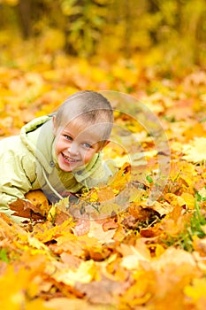 Boy in jacket lies in autumn yellow fallen leaves with pumpkins