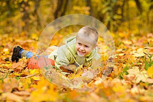 Boy in jacket lies in autumn yellow fallen leaves with pumpkins