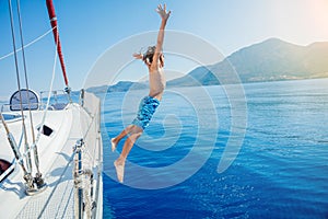 Boy jump of sailing yacht on summer cruise. Travel adventure, yachting with child