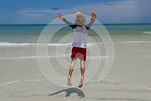 Boy jumping on the beach in front of ocean waves