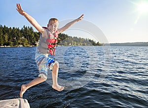 Boy jumping into a beautiful mountain lake. Having fun on a summer vacation