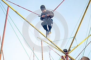 The boy is jumping on a bungee trampoline. A child with insurance and stretchable rubber bands hangs against the sky. The concept