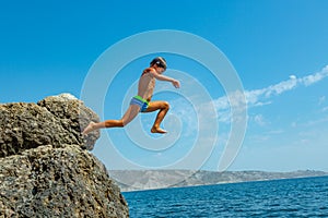 A boy is jumping from the cliff into the sea on a hot summer day. Holidays on the beach. The concept of active tourism