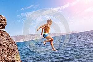 A boy is jumping from the cliff into the sea on a hot summer day. Holidays on the beach. The concept of active tourism