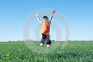 Boy jumping high, green grass and blue sky on the background,success, fortune, achievement and winning