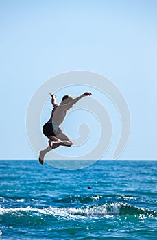 Boy jumping off cliff into the sea.