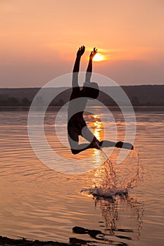 Boy jumping into water on sunset