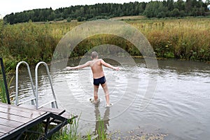 Boy jumping from wooden bridge into pond