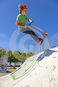 Boy jumps with his scooter at a skate park