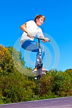 Boy jumps with his trick scooter in the skatepark