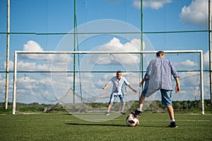Boy kicking a penalty at goal playing with his father on a green grass.