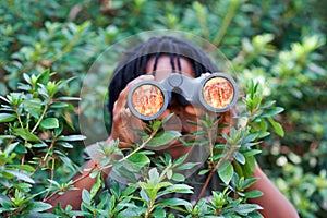 Boy, kid and binoculars for search in nature while learning and fun in forest or adventure at summer camp. Young African