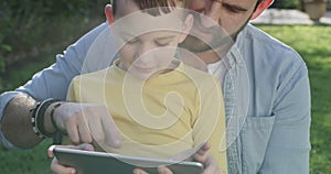 Boy kid, father and tablet in park for elearning, video games and reading ebook story on grass. Dad, child and download