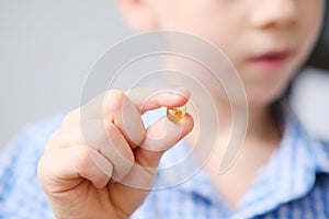 Boy kid holds a capsule with fish oil in gelatin in his hand, the concept of children`s health, avitaminosis, treatment