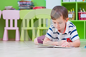 Boy kid lay down on floor and reading tale book in preschool li