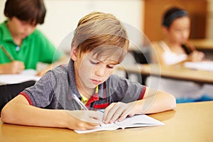 Boy kid, school classroom and writing test with focus, concentration and thinking for education goals. Male child, book