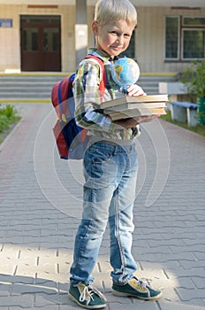 A boy with a knapsack, books and a globe goes to school after a long summer.