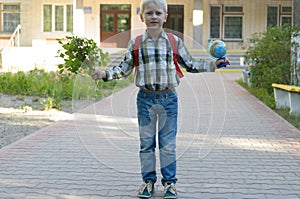 A boy with a knapsack, books and a globe goes to school after a long summer.