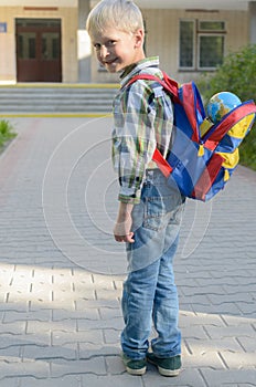 A boy with a knapsack, books and a globe goes to school after a long summer.