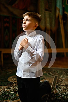 The boy is kneeling in prayer to God.